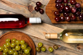 Red and white wine bottles alongside fresh red and green grapes, representing the rich diversity of Greek wines.