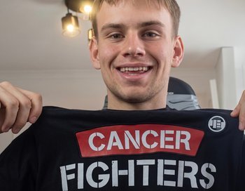 Piotr Hancke, known as Latwogang, smiling and holding a 'CANCER FIGHTERS' t-shirt, symbolizing his record-breaking 2026 charity stream for childhood cancer.