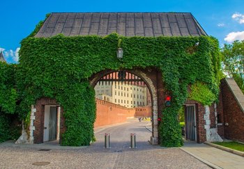 Arched red brick gate with green ivy in central Krakow, overlooking the city walls and historical buildings.