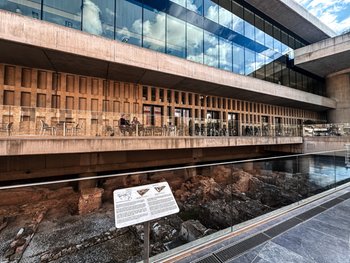 Nowoczesna szklana fasada Muzeum Akropolu w Atenach z widocznymi wykopaliskami pod szklaną podłogą przy wejściu.