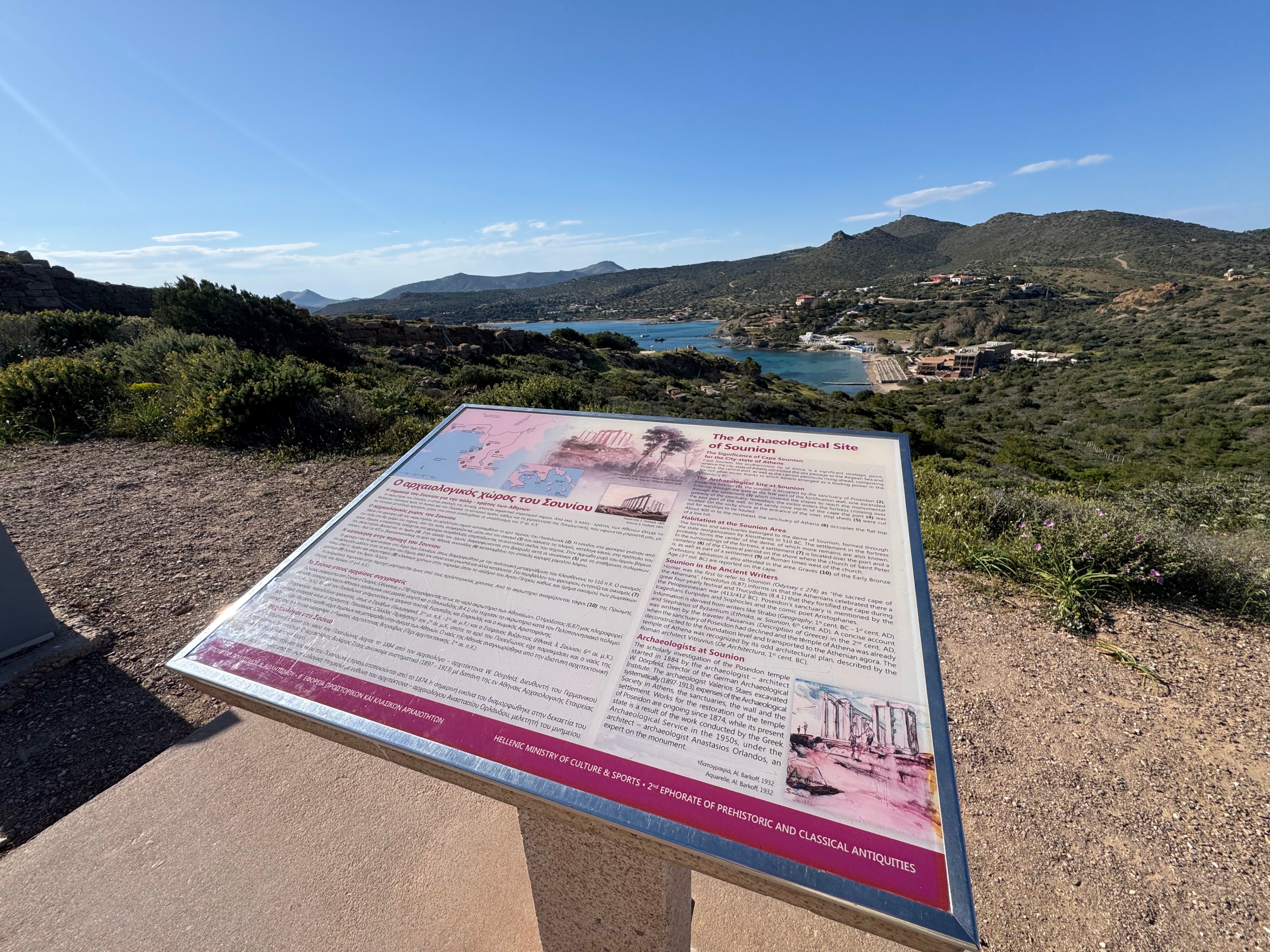Panoramiczny widok na Przylądek Sunion w Attyce z tablicą informacyjną, ukazujący zatokę, wzgórza i strategiczne położenie starożytnej fortecy.