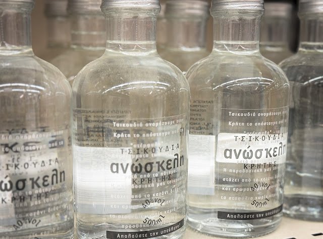 Clear bottles of Tsikoudia, also known as Cretan Raki, a strong Greek grape distillate, on a store shelf.