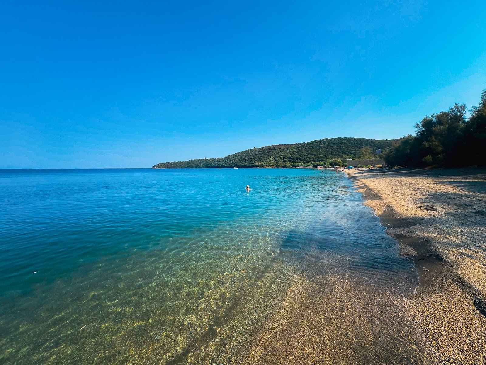 Spokojna plaża Vathy w Gythio na Peloponezie, z krystalicznie czystą turkusową wodą i zielonymi wzgórzami w tle.